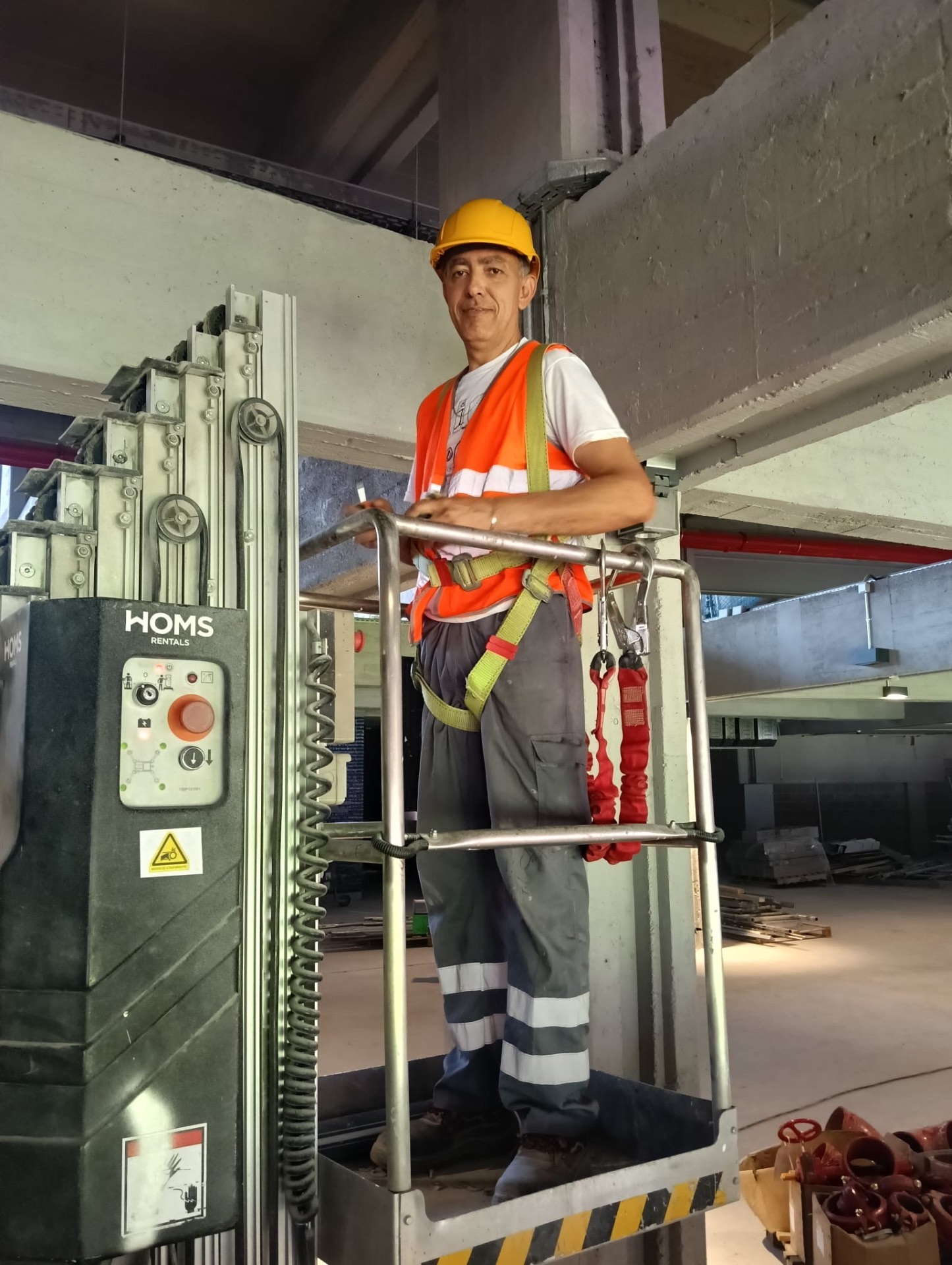 Trabalhador com capacete, colete refletor e arnês numa plataforma elevatória